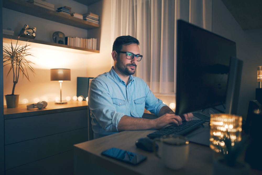 Modern young man working remotely from home at night.